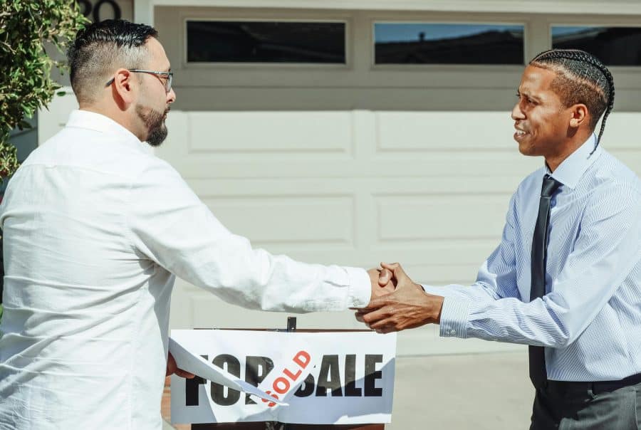 Two men shaking hands, sold sign
